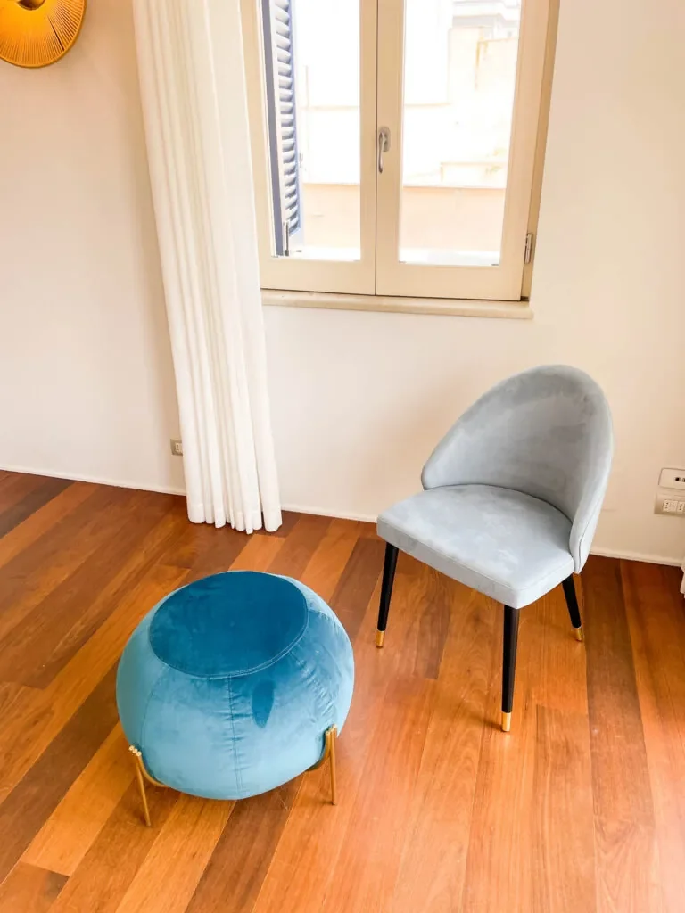 Poltroncina grigia e pouf blu di Fos vicino alla finestra