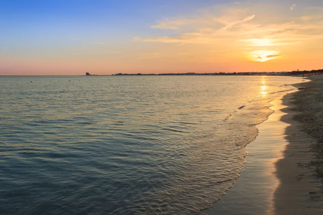 Spiaggia sabbiosa pugliese al tramonto, con il sole basso sul mare calmo